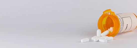 Orange pill bottle spilling white pills onto a table