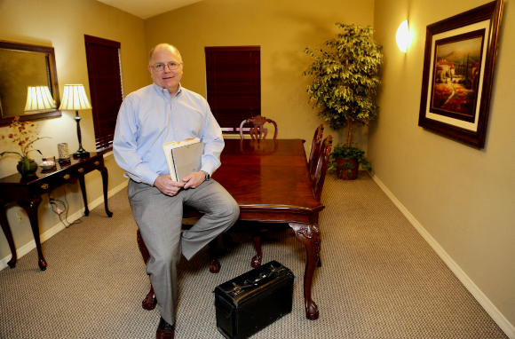 Attorney Mark A. Cornelius Sitting on a Table and Holding Documents