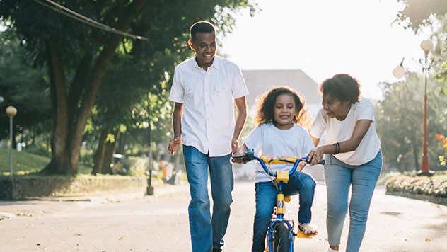 Family in a street teaching the daughter how to ride a bike