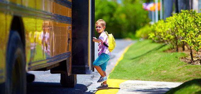 Young boy with yellow backpack getting onto school bus