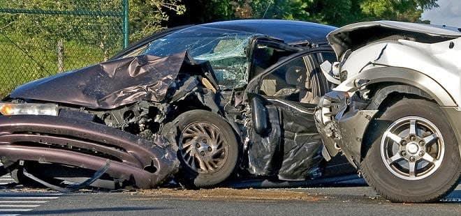 Black car totaled with a silver car perpendicular to it with damage to the front