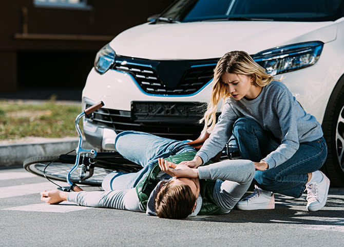 A woman helping a bicyclist that she recently hit with her car.