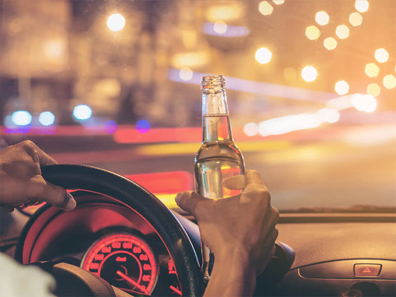 Person driving a car while drinking out of a bottle