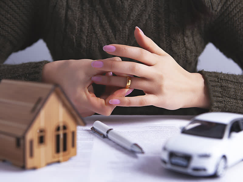 Woman holding her wedding ring near a tiny model of a house and car
