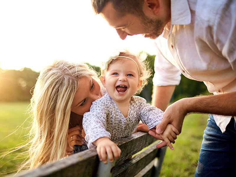 Two parents and their baby play on a park bench at sunset
