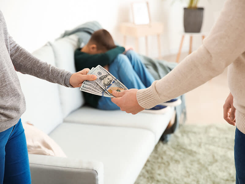 Man paying his ex-wife child support while a young boy looks sad in the background
