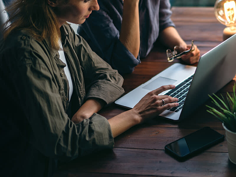 Two businesswoman working together on a laptop with a lamp on nearby