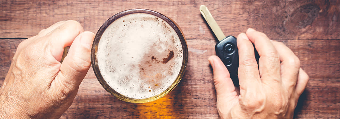 Person sitting and holding car keys and amber colored drink