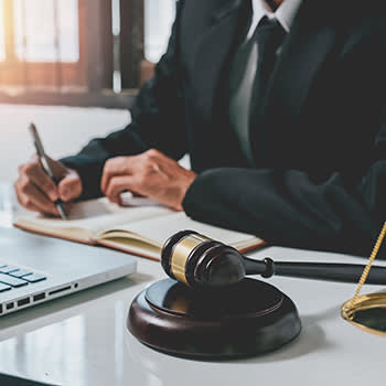 Man in suit writing on a document with a gavel on his desk