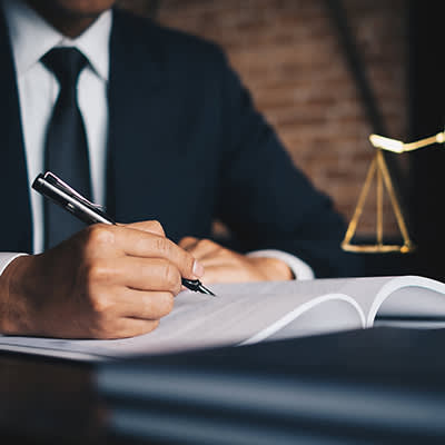man in suit writing in a book with justice scale next to him