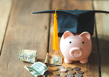 A piggy bank wears a graduation cap with money in front of it