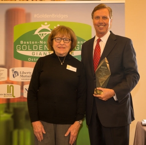 Tall man in suit holding an award smiling for picture with a woman