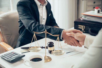 Two people shaking hands next to a cup of coffee and scales of justice