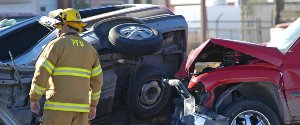 Firefighter standing near a car accident with a car turned over on its side-1