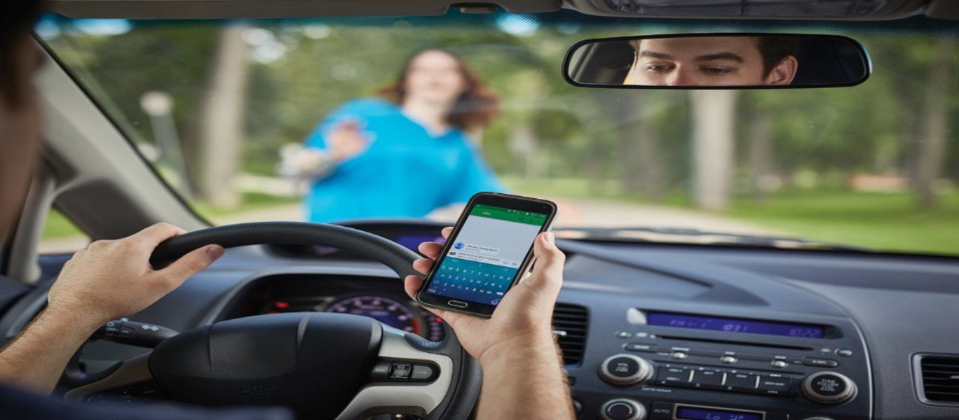 Distracted driver looking at his phone with a woman directly in front of his car