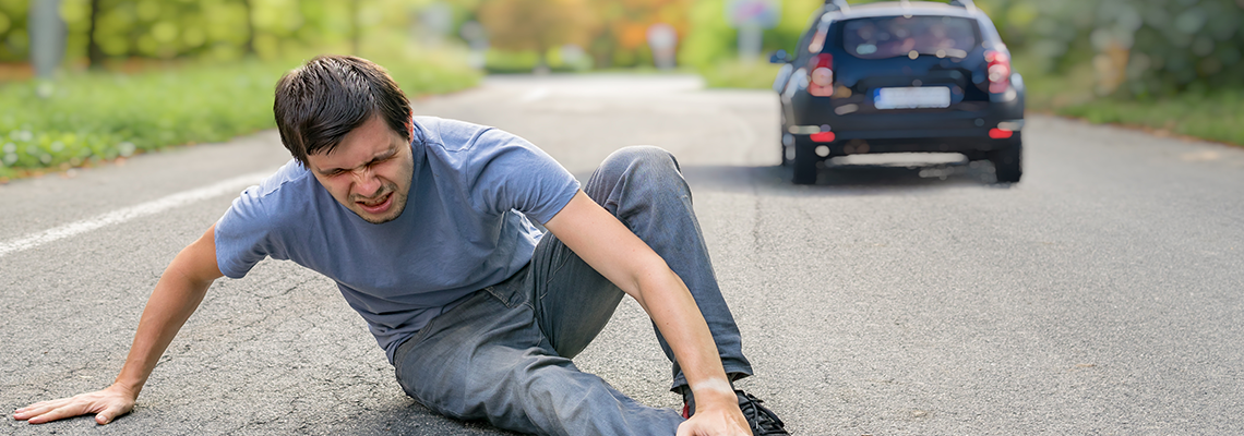 Person in road holding leg with car in background