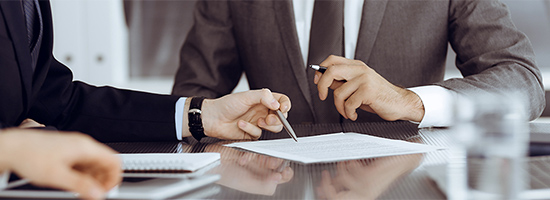 Two people in suits sitting at table with paper and pens