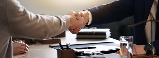 Two people shaking hands over a desk with paperwork