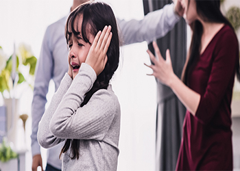 Child crying with hands over ears with adults in background