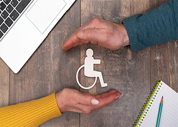 Paper model of person in wheelchair on desk with hands