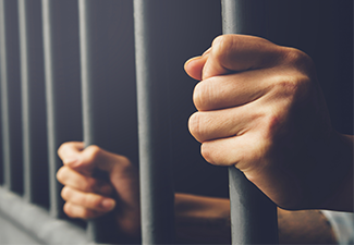 Man in prison hands of behind hold Steel cage jail bars. 