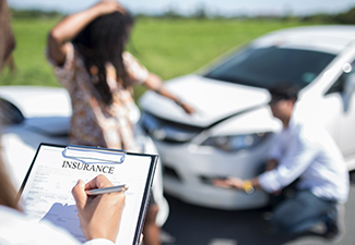 Side view of writing on clipboard while insurance agent examining car after accident