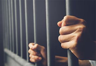 Man in prison hands of behind hold Steel cage jail bars. 