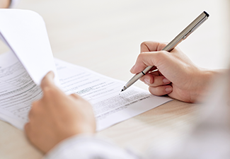 Crop shot of person with pen signing contract at desk in daylight