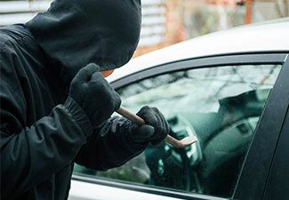 Close-up of a thief wearing balaclava breaking car window with crowbar. 