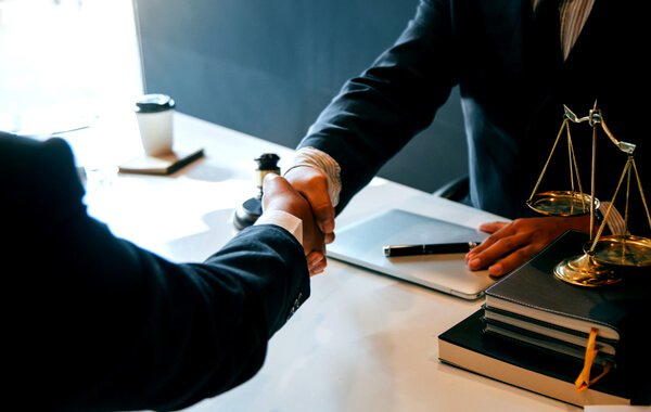 Two businessmen shaking hands by scales of justice