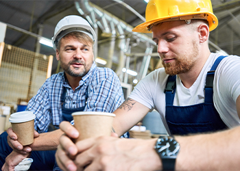 Two people in construction hats sitting and drinking coffee