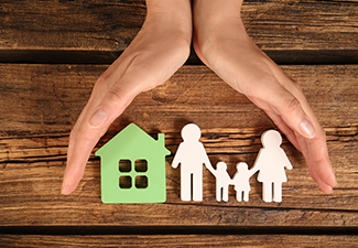 Two hands protecting paper cutouts of a home and family