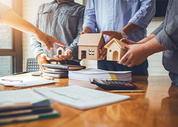 People in suits standing around desk with model houses