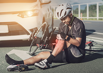 Person on the ground next to car holding knee in pain