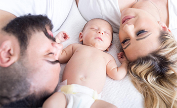 Two people laying on bed with small baby