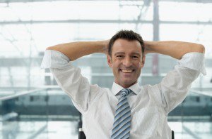 Man with tie smiling with arms behind head