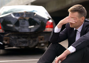 Desperate man sitting asphalt on crashed car background