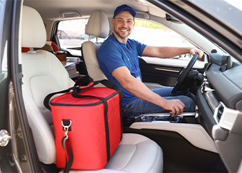 Person in car smiling next to food delivery bag