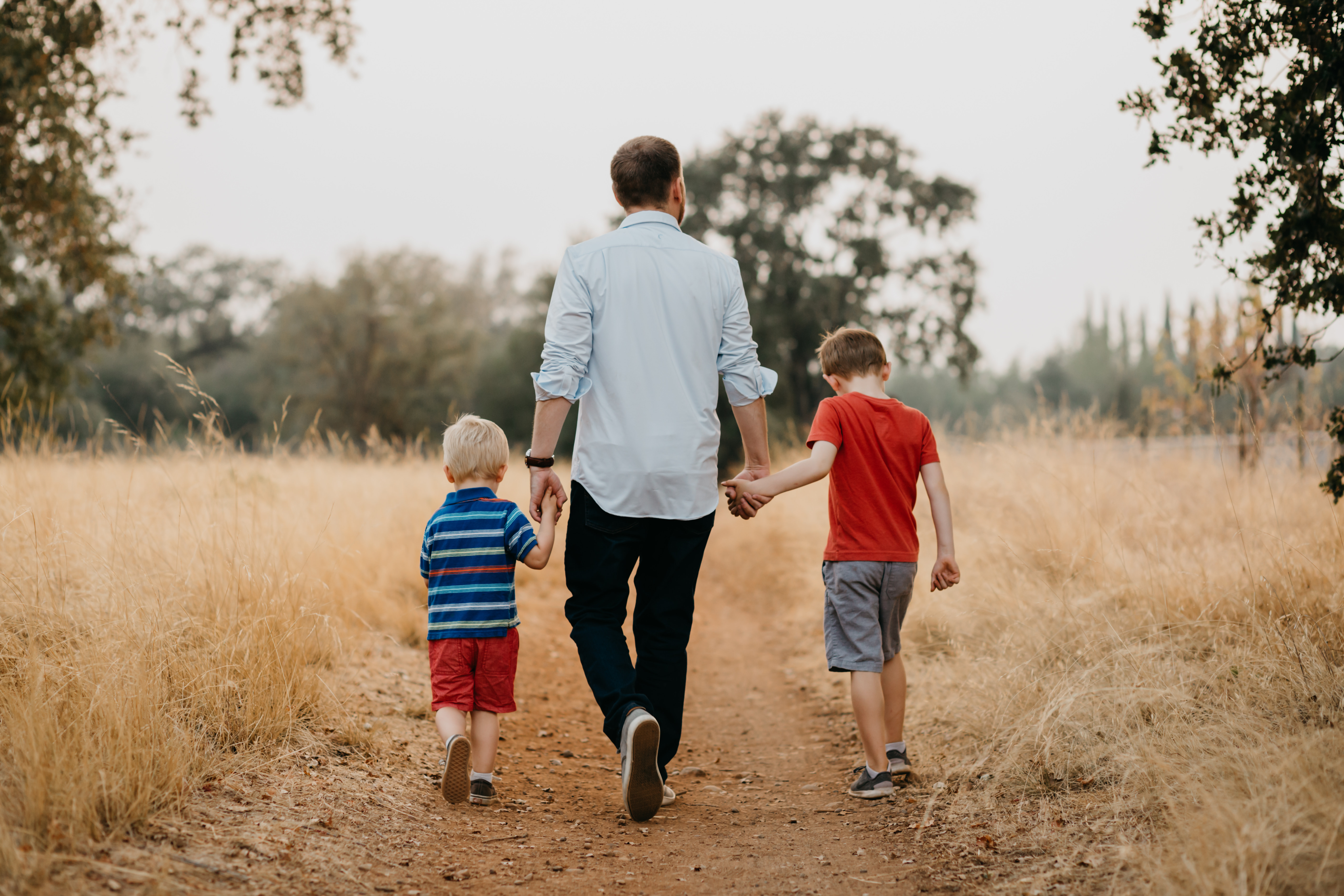 dad holding hands with his two sons while walking down a gravel trail in the middle of a field