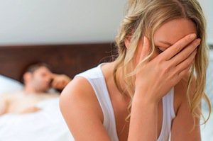 Worried woman at foot of bed with man in bed