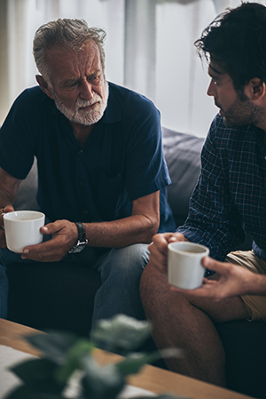 Elderly man and younger man talking with cups of coffee