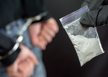 Person holding bag with powder next to person in handcuffs