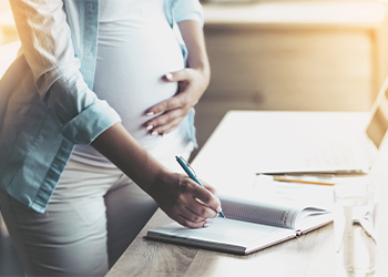 Person who is pregnant writing at desk with computer