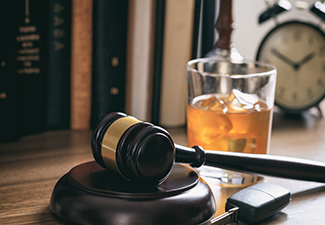 Law gavel alcohol and car keys on a wooden desk.