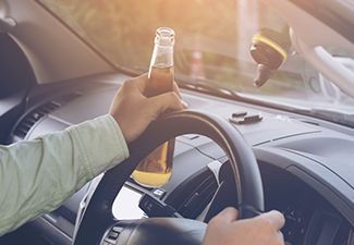 Drunk young man drives a car with a bottle of beer.