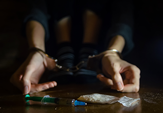 Syringe and Drugs with A Defocused Man Handcuffed on The Floor