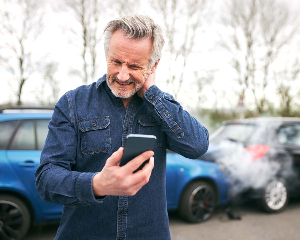 Male Driver With Whiplash Calls Car Insurance Company On Mobile Phone After Traffic Accident