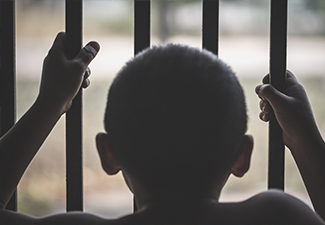 Hands of a young child clutching prison bars.