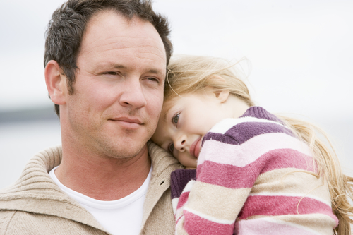 A young daughter resting her head on her father's shoulder.