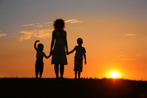 A mom holding her children's hands at sunset.